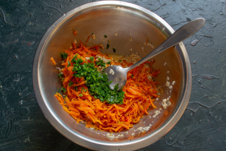Adding fresh herbs to the Ovsyanoblin batter Adding freshly chopped parsley to the carrot and oatmeal mixture in a bowl.