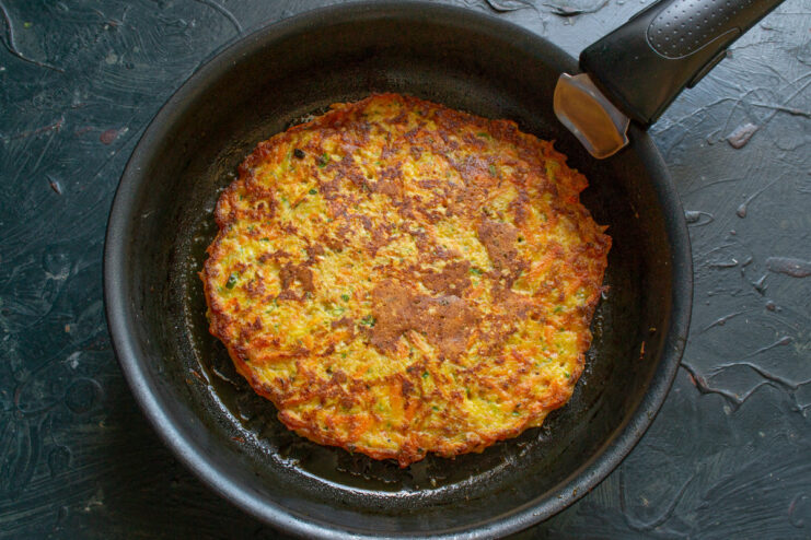 Flipping the delicate Ovsyanoblin pancake Using a wide spatula to carefully flip the golden-brown Ovsyanoblin in the frying pan.