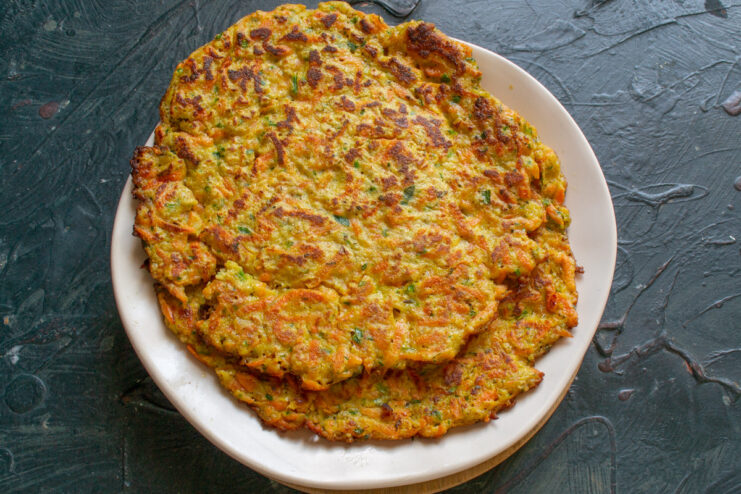 Cooking a batch of savory oatmeal pancakes A freshly cooked Ovsyanoblin on a plate next to the pan where another one is cooking.