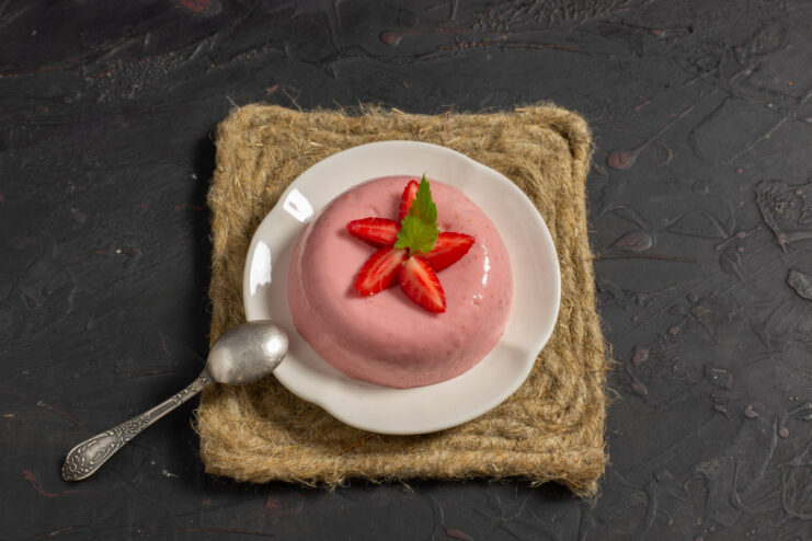 Final Step: Garnishing and Serving Strawberry Panna Cotta A finished strawberry panna cotta on a plate, garnished with a fresh strawberry and a lemon balm leaf.