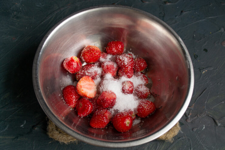 Step 3: Preparing the Strawberry Base A bowl of fresh, washed strawberries with granulated sugar being added on top.