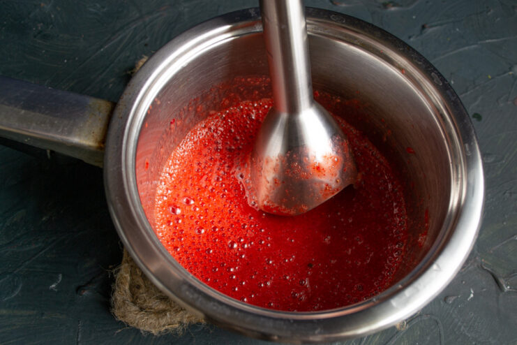 Step 4: Blending Strawberries into a Smooth Puree An immersion blender pureeing strawberries and sugar in a bowl until smooth.