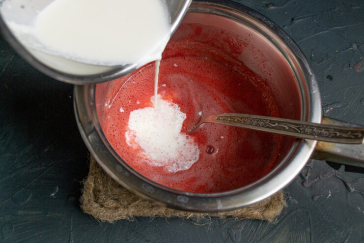 Step 7: Combining Cream Mixture with Strawberry Puree Pouring the white cream and milk mixture into the hot strawberry puree in a saucepan.