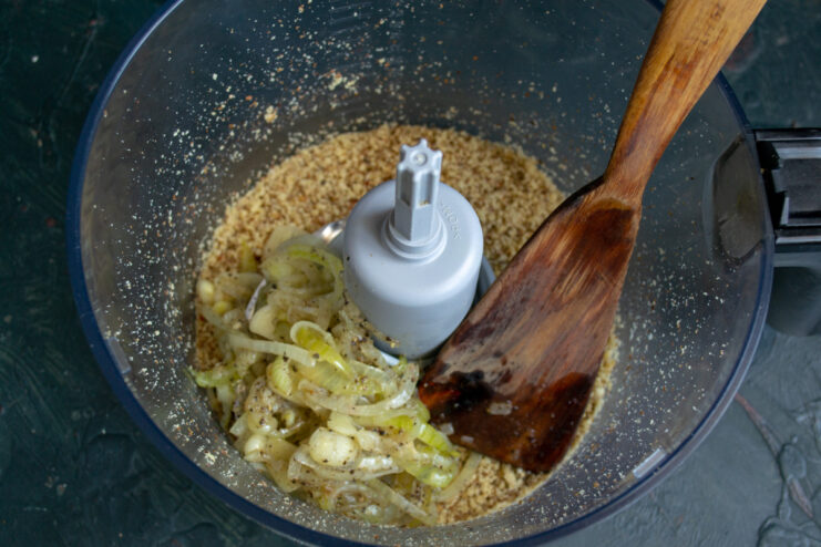 Combining Ingredients in the Blender Sautéed onions and garlic being added to ground walnuts in a blender bowl.