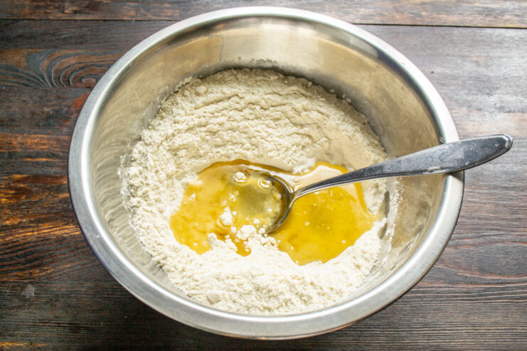 Adding Vegetable Oil to the Flour Mixture Pouring refined vegetable oil from a measuring cup into the bowl of sifted flour.