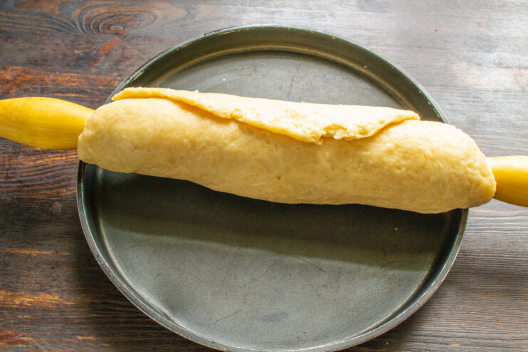 Using a Rolling Pin to Transfer the Dough A thin sheet of rolled-out pie dough being carefully wrapped around a wooden rolling pin.