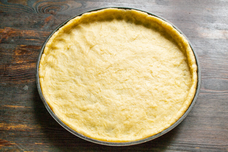 Lining the Baking Pan with Pastry Dough Hands pressing the pastry dough evenly into a round metal baking pan.