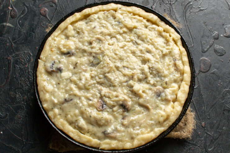 Step 8: Assembling the pie with the mushroom filling The creamy mushroom filling being spread evenly over the pie crust in a baking dish.