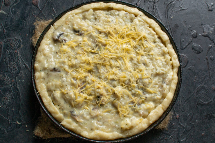 Step 9: Topping the pie with cheese before baking Grated cheese being sprinkled over the mushroom filling in the pie.