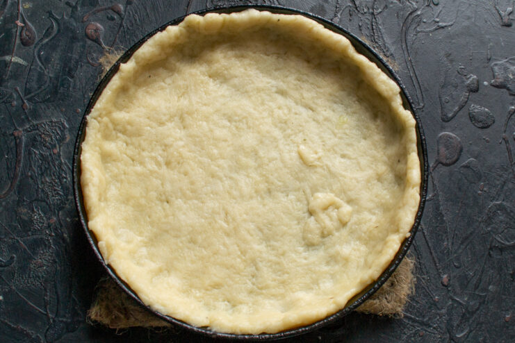 Step 4: Lining the baking dish with the rolled-out dough Rolled-out pie dough being placed into a round baking dish.