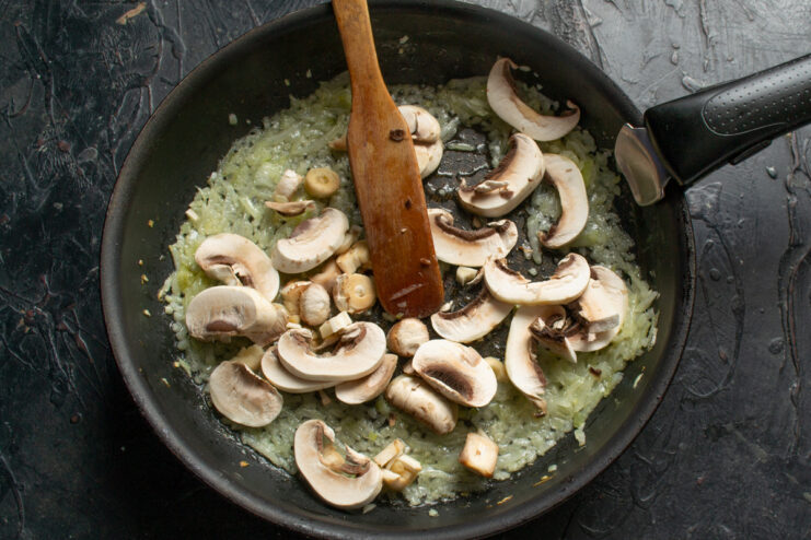 Step 6: Cooking the mushrooms for the pie filling Sliced champignon mushrooms being added to the pan with sautéed onions.