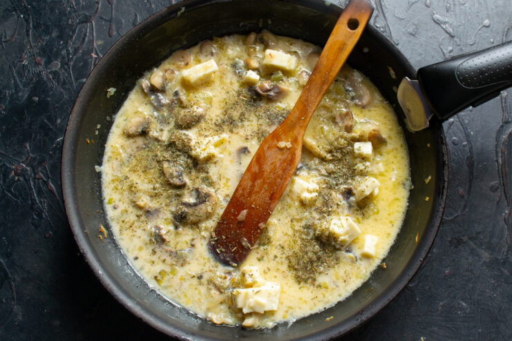 Step 7: Creating the creamy sauce for the filling A creamy sauce being poured over cooked mushrooms and onions in a pan.