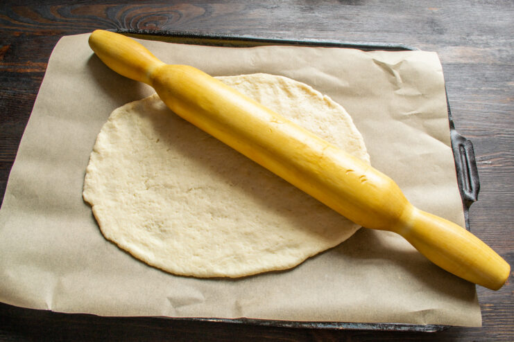 Rolling Out the Bottom Crust for the Pie Rolling out a piece of dough into an oval shape on parchment paper.