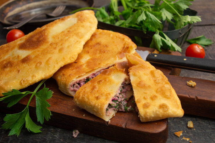 A plate of golden-brown, pan-fried pirozhki with a meat filling.