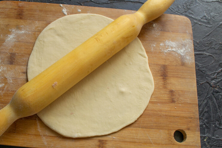 Rolling Out the Pirozhki Dough A ball of dough being rolled out into a thin circle on a floured board.