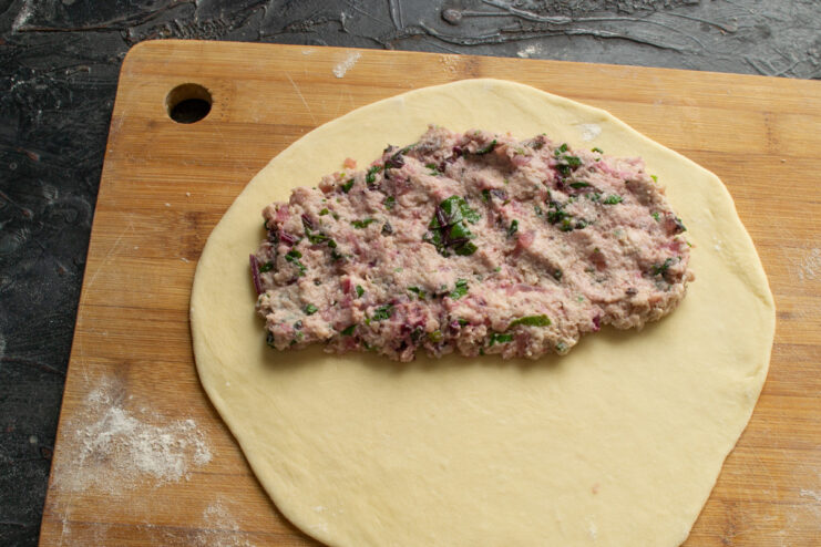 Assembling the Pirozhki: Adding the Filling Meat filling spread over one half of a rolled-out circle of dough.
