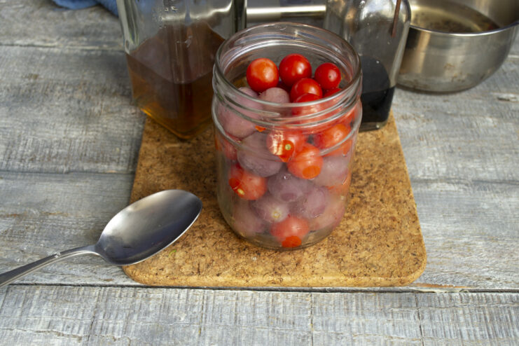 Adding Vinegar for Tang and Preservation Pouring vinegar from a small measuring cup into the jar of tomatoes and grapes.