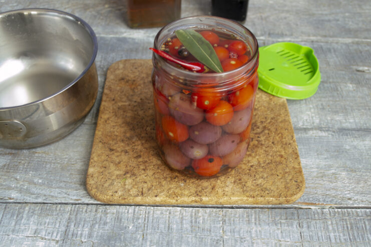 Filling the Jar with Hot, Spiced Brine Pouring the hot, spiced brine from a saucepan into the jar over the tomatoes and grapes.