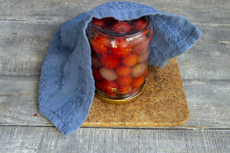 Sealing the Jar to Ensure Freshness A hand tightly screwing a metal lid onto the glass jar of pickled tomatoes and grapes.