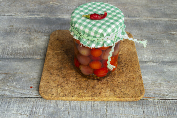 Storing Your Preserves and Enjoying Them Later A sealed jar of tomatoes with grapes turned upside down on a wooden surface to cool.