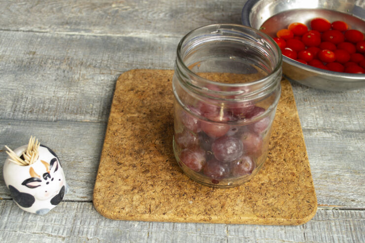 How to Prepare Grapes for Pickling Hands plucking fresh pink grapes from their stems into a white bowl.