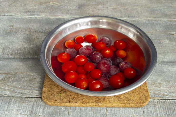 Washing Tomatoes and Grapes Before Canning A white bowl with cherry tomatoes and grapes being washed under water.
