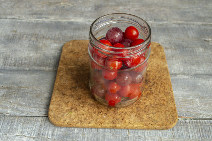 Packing the Jar Tightly for Best Results A glass canning jar being tightly packed with layers of cherry tomatoes and pink grapes.