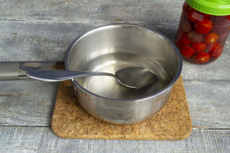 Draining the Water to Create the Brine Pouring hot water from the jar of tomatoes and grapes into a stainless steel saucepan.