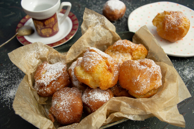 A plate of freshly made choux pastry doughnuts, golden brown and dusted with white powdered sugar.
