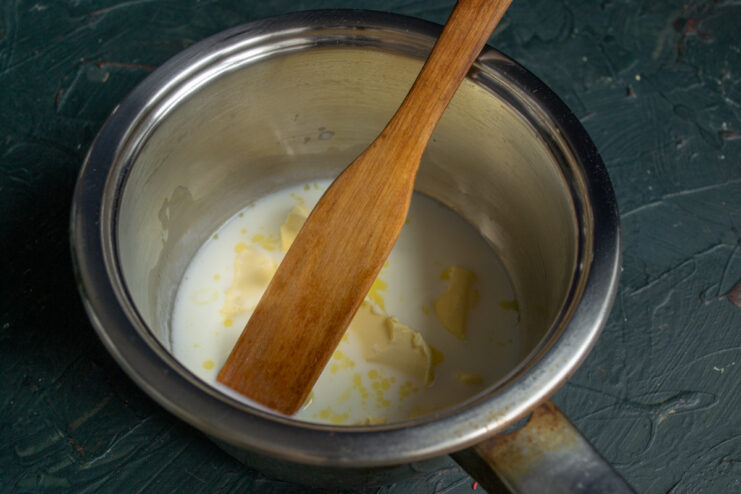 Starting the Choux Pastry: Melting Butter and Milk A saucepan on a stove with milk, butter, and salt being heated to a boil for choux pastry.