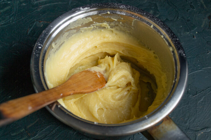 Mixing the Choux Pastry Dough to the Right Consistency A thick choux pastry dough being mixed with a spatula in a saucepan.