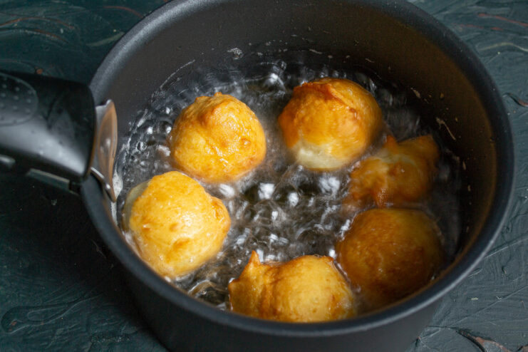 Frying the Choux Doughnuts to Golden Perfection Several choux pastry doughnuts frying in a saucepan of hot oil, puffing up and turning golden.