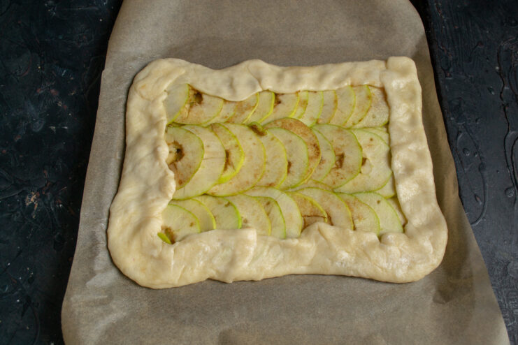 Sprinkling the Assembled Galette with Sugar and Cinnamon Before Baking Sprinkling sugar and cinnamon over the folded apple galette.
