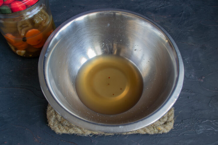 Pouring pickle brine from a glass jar into a white ceramic bowl.