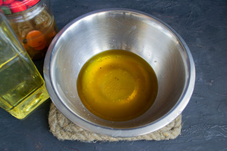 Adding olive oil to the bowl with pickle brine.
