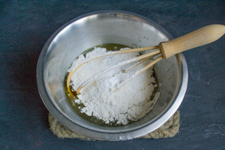 Adding all-purpose flour and baking powder to the wet ingredients in the bowl.