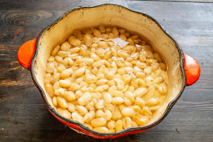 Cooking Beans in a Cast-Iron Pot for Even Heat White beans simmering in a black cast-iron pot on a stove.