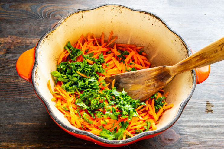 Adding Fresh Parsley for Flavor and Aroma Finely chopped fresh parsley being added to grated carrots in a pot.