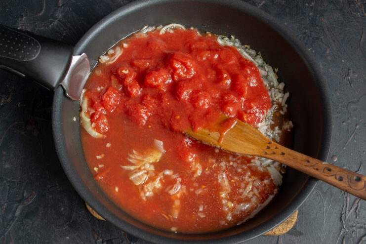 Adding Canned Tomatoes to Create the Sauce Diced canned tomatoes being added to a pan with sautéed onions for the sauce.