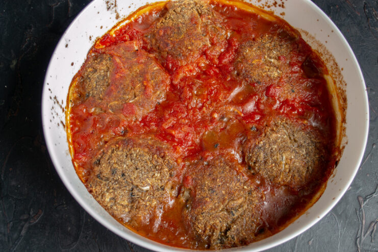 Garnishing the Baked Cabbage Patties Before Serving Baked cabbage patties in tomato sauce in a dish, garnished with fresh green herbs.