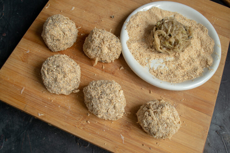 Shaping and Breading the Cabbage Patties Hands shaping a cabbage patty and coating it in a plate of breadcrumbs.
