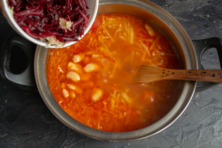 Adding Beets and Garlic for Color and Flavor Grated cooked beetroot and minced garlic being added to the pot of borscht.