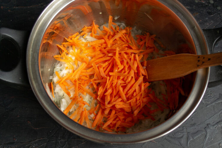 Grating Carrots for the Soup Base A hand grating a fresh carrot on a box grater for the borscht.