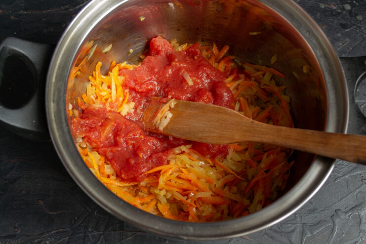 Adding Tomatoes for Acidity and Richness Canned chopped tomatoes being added to the sautéed onions and carrots in a pot.