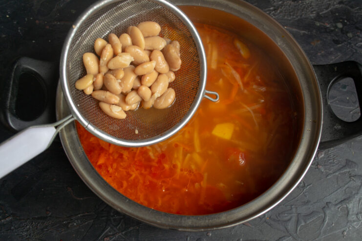 Adding Beans for Protein and Texture Canned beans being added from a can into the simmering borscht.