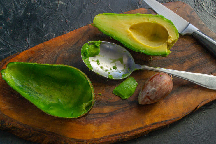 How to Prepare an Avocado for Stuffing A ripe avocado cut in half, with the pit still in one half, on a wooden cutting board.