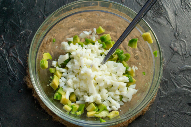 Adding Diced Egg White to the Avocado Filling Diced hard-boiled egg white being added to a bowl of diced avocado.