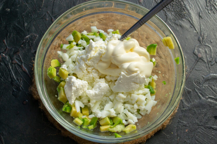 Making the Creamy Filling for Stuffed Avocados Adding a spoonful of cream cheese and mayonnaise to the bowl with avocado and egg.