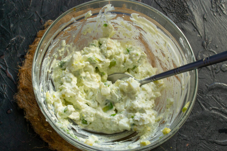 Seasoning the Avocado and Egg Filling Seasoning the avocado filling in a white bowl with salt and pepper.