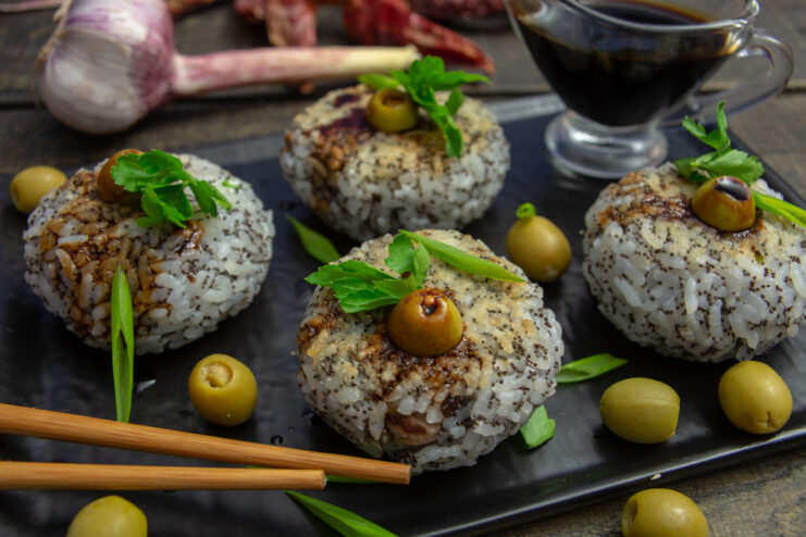 A plate of stuffed rice balls drizzled with teriyaki sauce and garnished with olives and green onions.